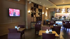 Um restaurante com mesas e cadeiras de madeira, uma tela de televisão e um balcão com um cardápio.