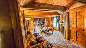 Interior acogedor de una cabaña de troncos con una cama, un sofá, una chimenea y una puerta de madera grande.