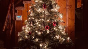 Un árbol de Navidad con luces y adornos, un reloj en la pared y una escalera de madera.