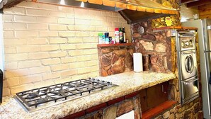 Una cocina con estufa a gas, pared de piedra y horno empotrado.
