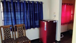 Una habitación con dos sillas estampadas, un armario rojo y una cortina azul.