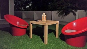 Un pequeño espacio al aire libre con una mesa de madera y dos sillas rojas.