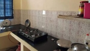 Una cocina con estufa a gas, un lavamanos y un ventanal con cortina.