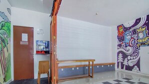 A room with a checkered floor, a wooden bench, a door with a bulletin board, and a wall with a colorful mural. - OYO 89994 Kartini House (Jakarta)