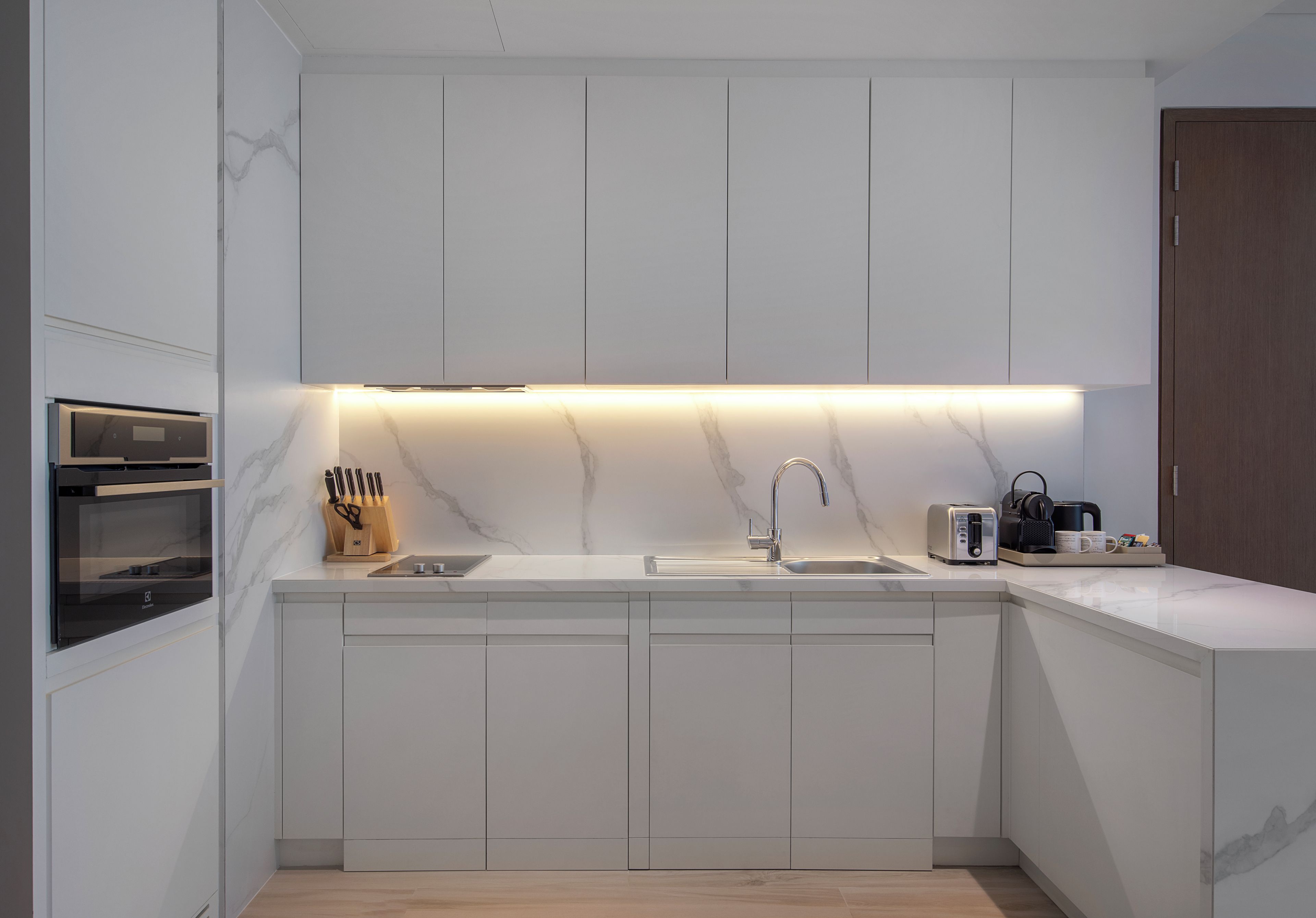 Eine moderne Küche mit weißen Schränken, einem Backofen, einer Spüle und einer Arbeitsplatte mit Kaffeemaschine und Toaster.