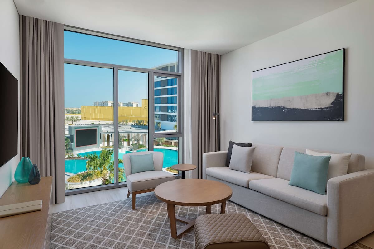 A modern hotel room with a large window, a sofa, a coffee table, and a painting on the wall.