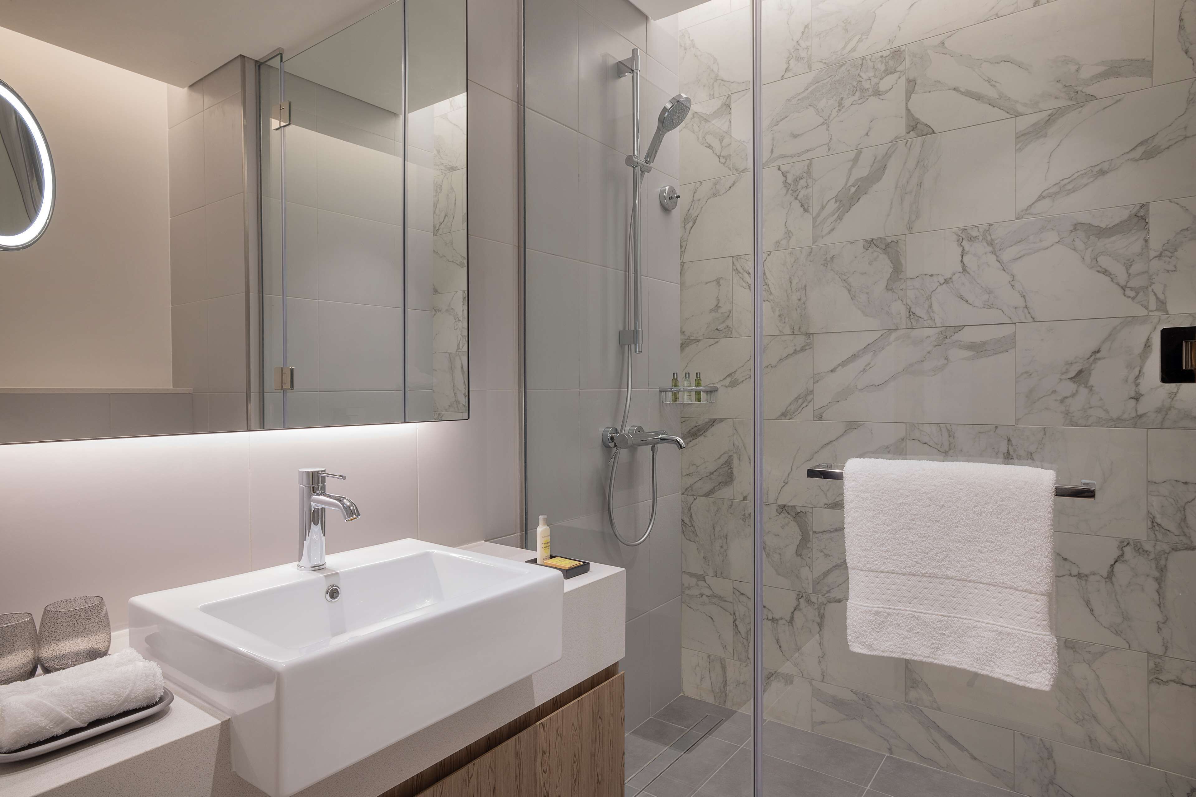A modern bathroom with a large mirror, a sink, and a shower.