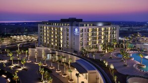 A modern hotel with multiple floors, a swimming pool, and a landscaped courtyard with palm trees.