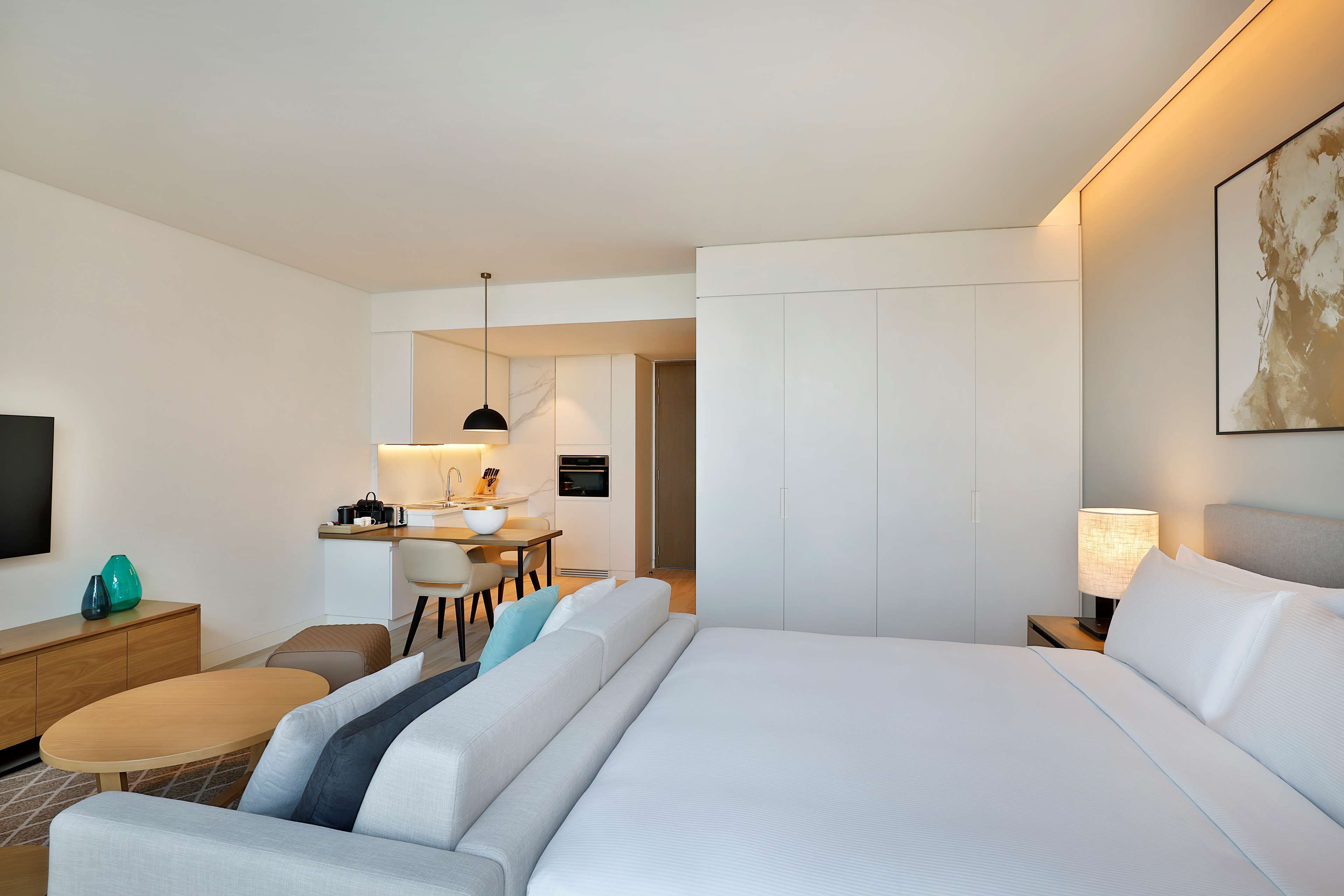 Une chambre d’hôtel avec un grand lit, un bureau avec une chaise, une petite table ronde, un téléviseur et un tableau au mur.
