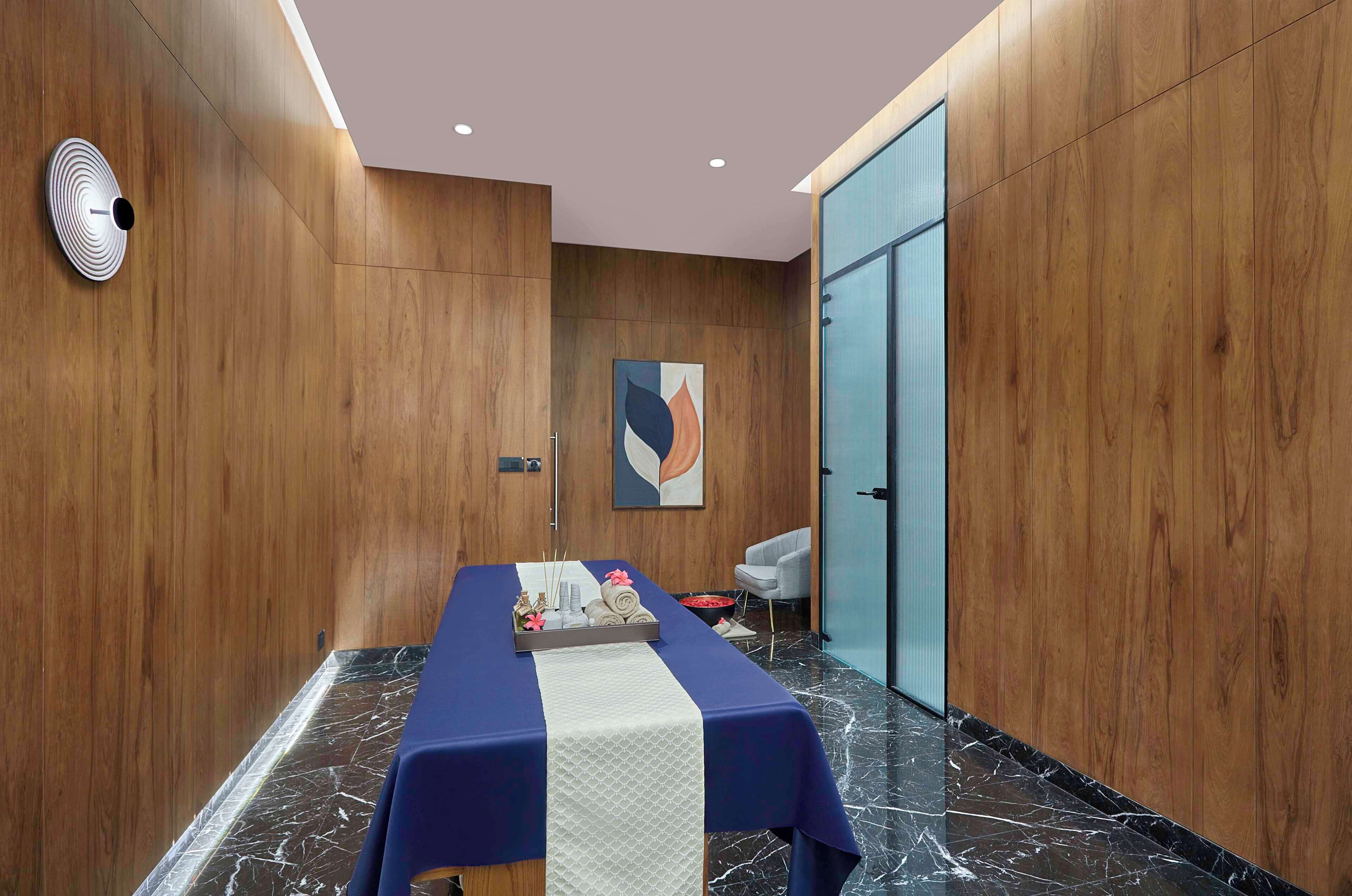 A room with a massage table, wooden panel walls, a blue door, and a marble floor.