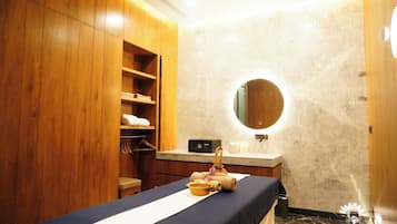 A hotel bathroom with a wooden wardrobe, a round mirror, a sink, and a massage table.