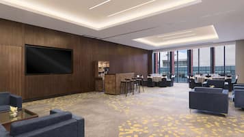 A modern hotel lobby with a large flat-screen TV, a bar area, and multiple seating options.