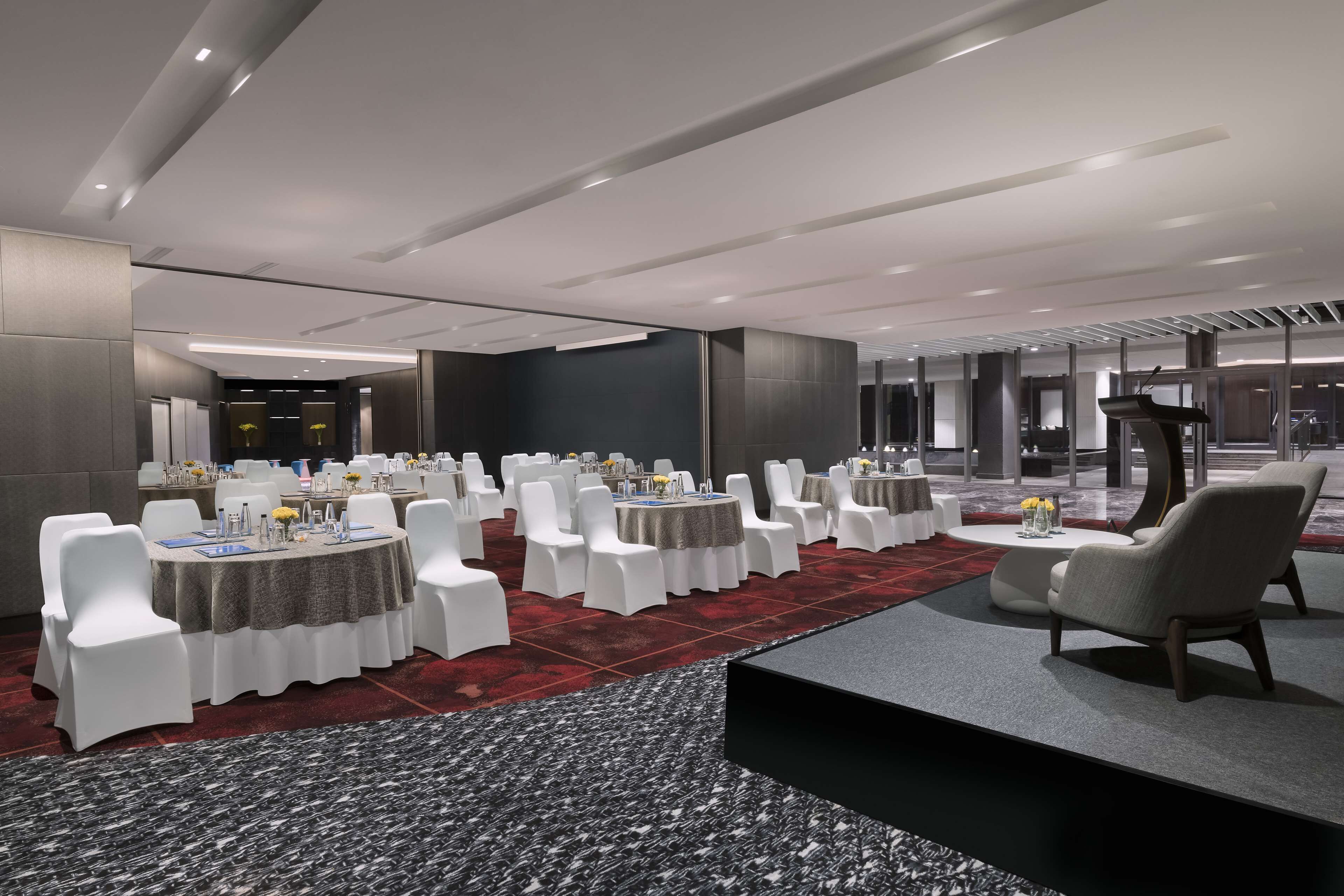 A modern conference room with round tables, white chairs, and a carpeted floor.