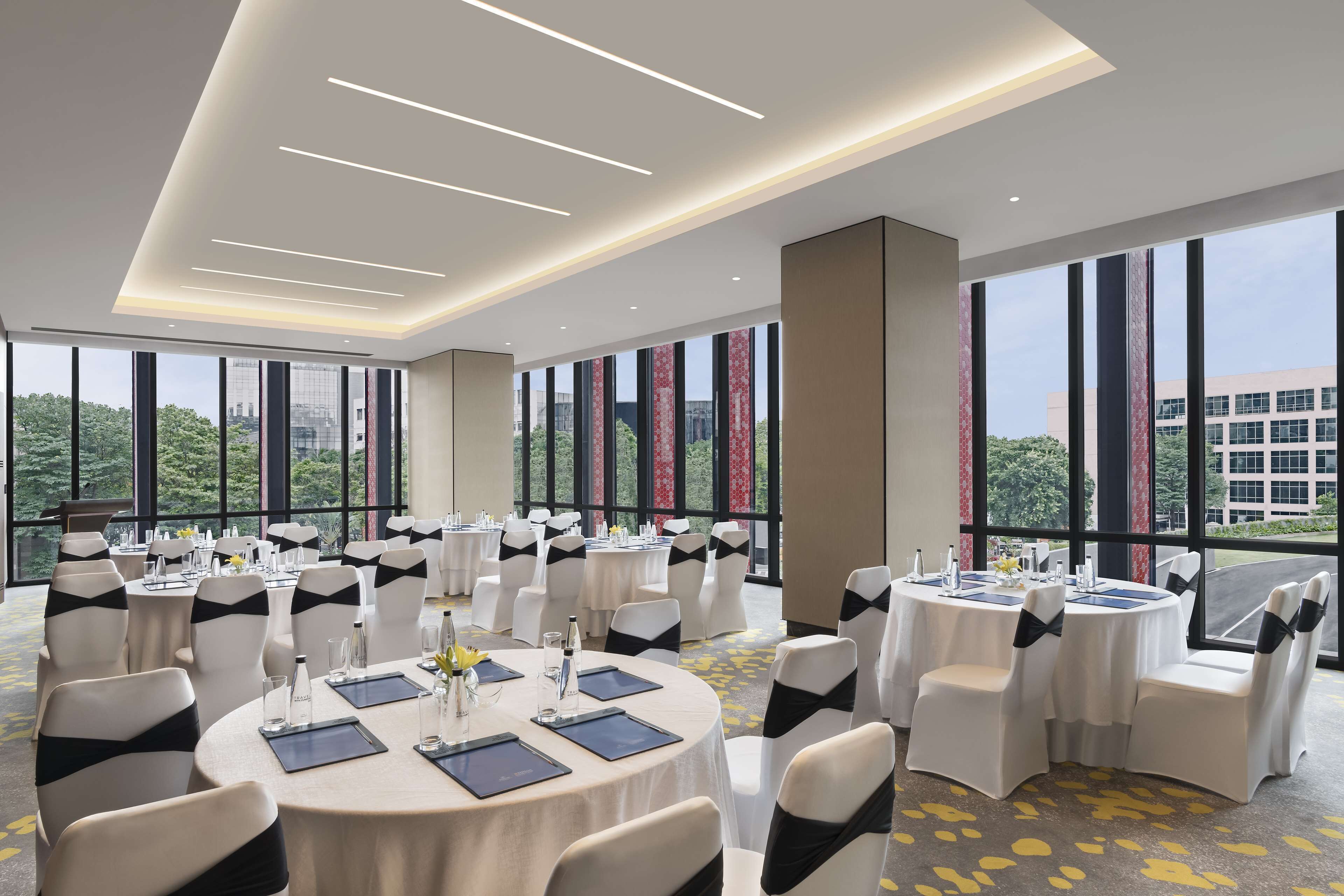 A conference room with round tables, white chairs with black sashes, and large windows offering a city view.