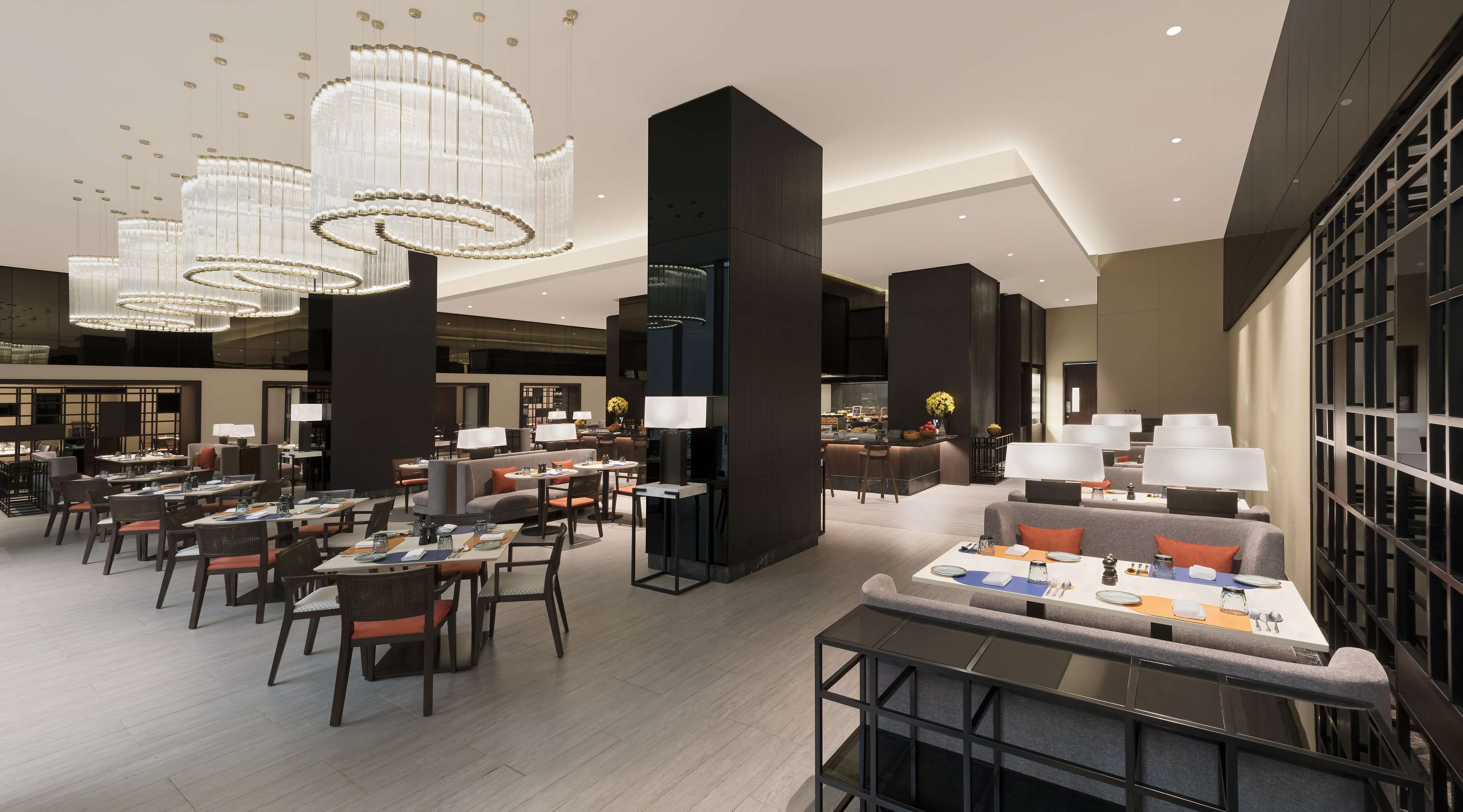 A modern hotel lobby with multiple seating areas, including a bar and dining tables, and a large chandelier.