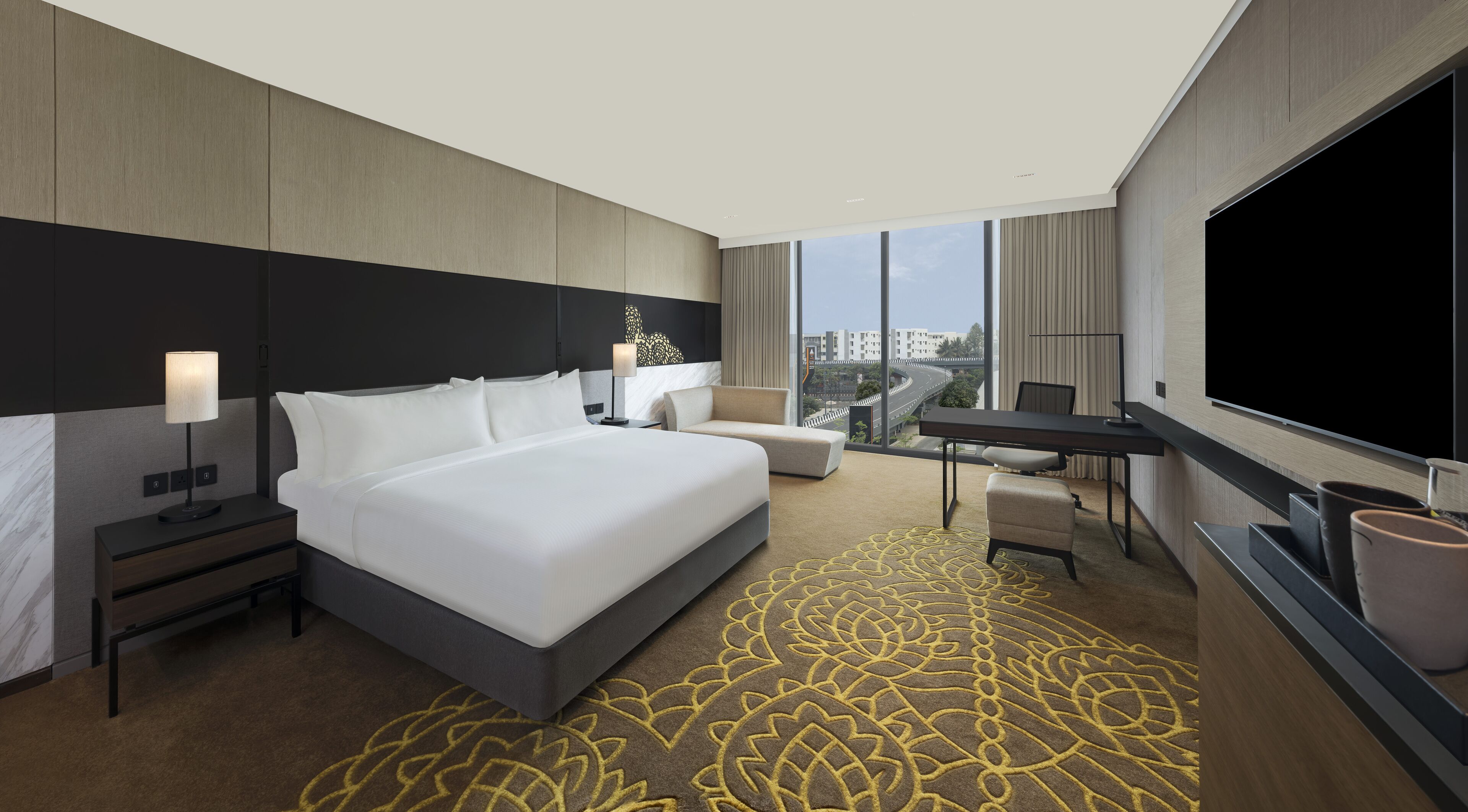 A modern hotel room with a large bed, a desk, a TV, and a view of the city.
