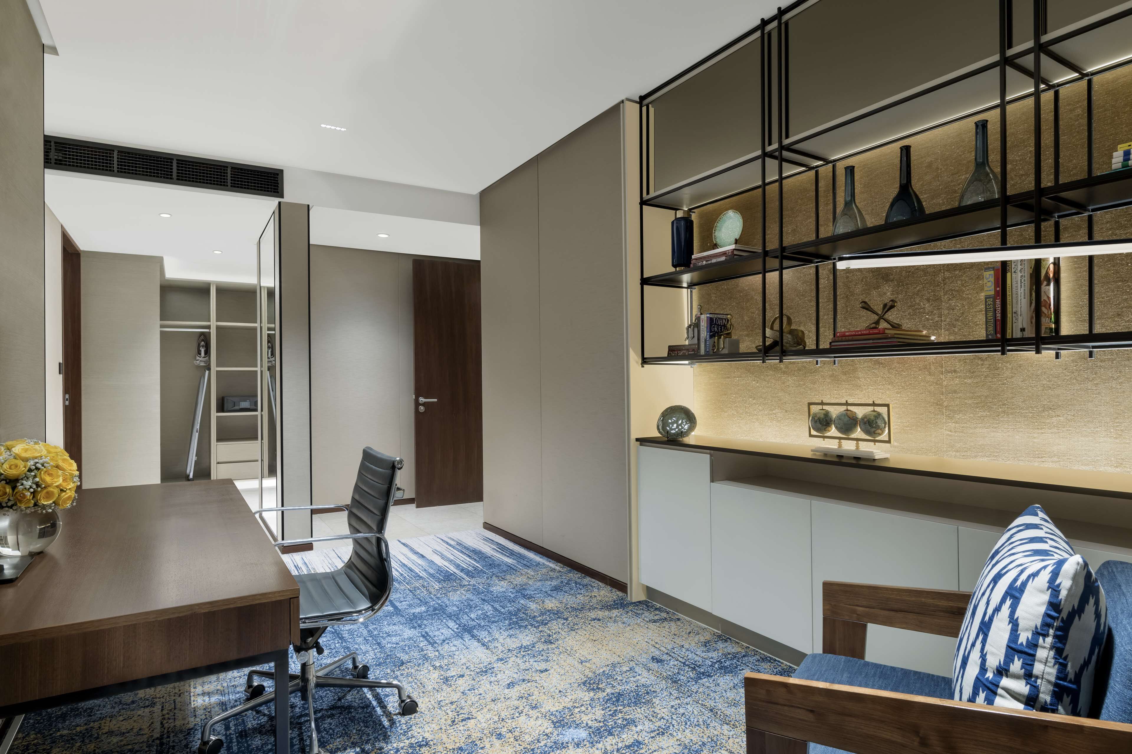 A modern conference room with a wooden table, a blue patterned carpet, a bookshelf with decorative items, and a door leading to a closet.