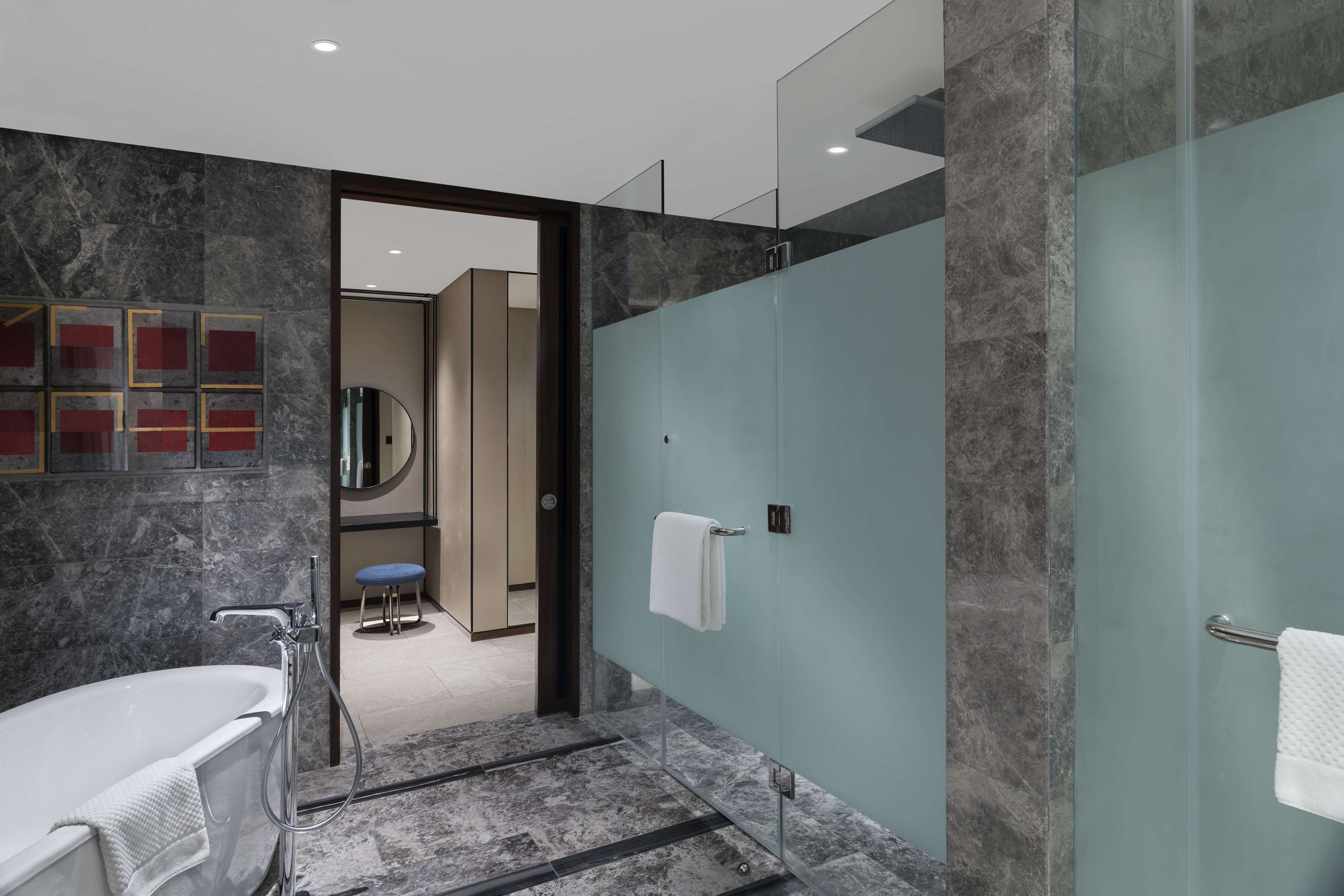 A modern bathroom with a bathtub, glass shower enclosure, and marble walls.