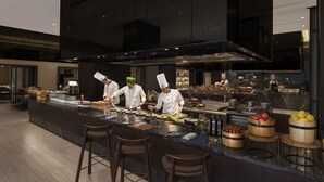 A modern kitchen with chefs preparing food, a marble countertop, and bar stools. - Hilton Bengaluru Embassy Manyata Business Park (Bengaluru)