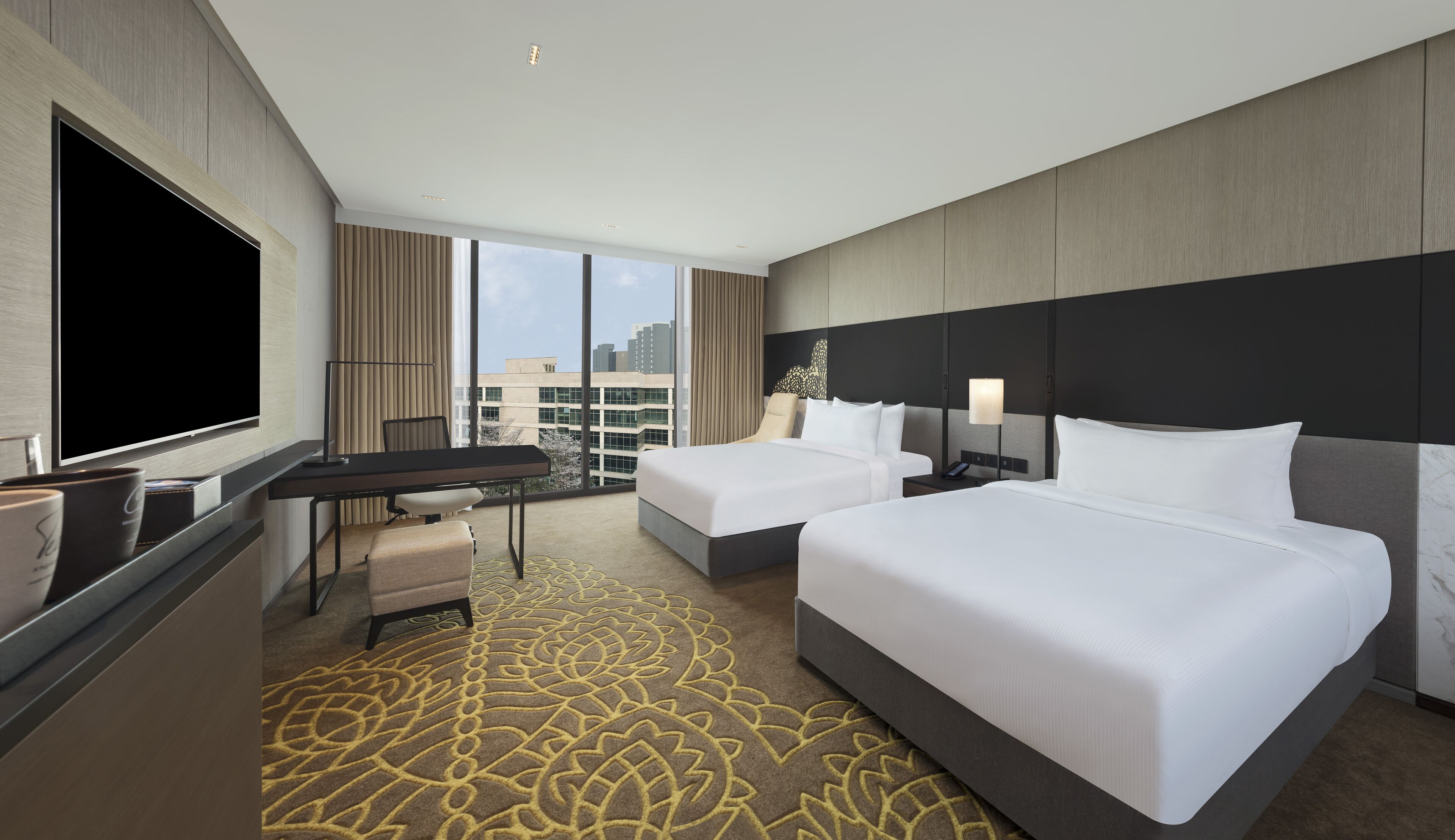 A hotel room with two beds, a desk, a TV, and a large window offering a city view.