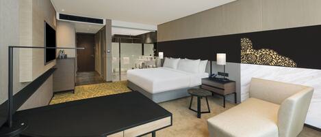A modern hotel room with a bed, a desk, a chair, a small table, a bathroom, and a decorative wall piece.