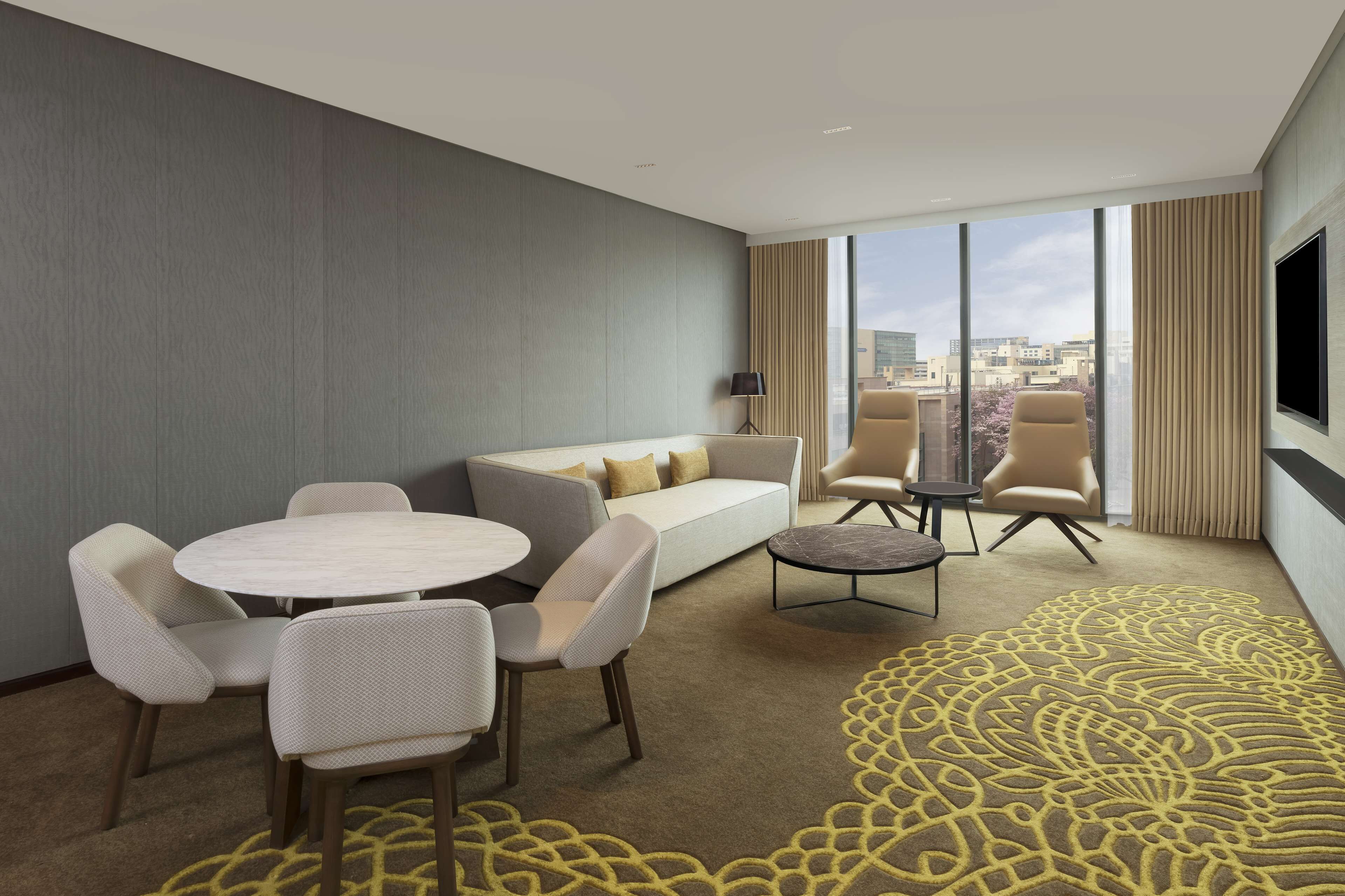 A modern hotel room with a sofa, chairs, a round table, and a TV.