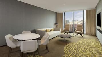 Una habitación de hotel moderna con sofá, sillas, una mesa redonda y televisión.