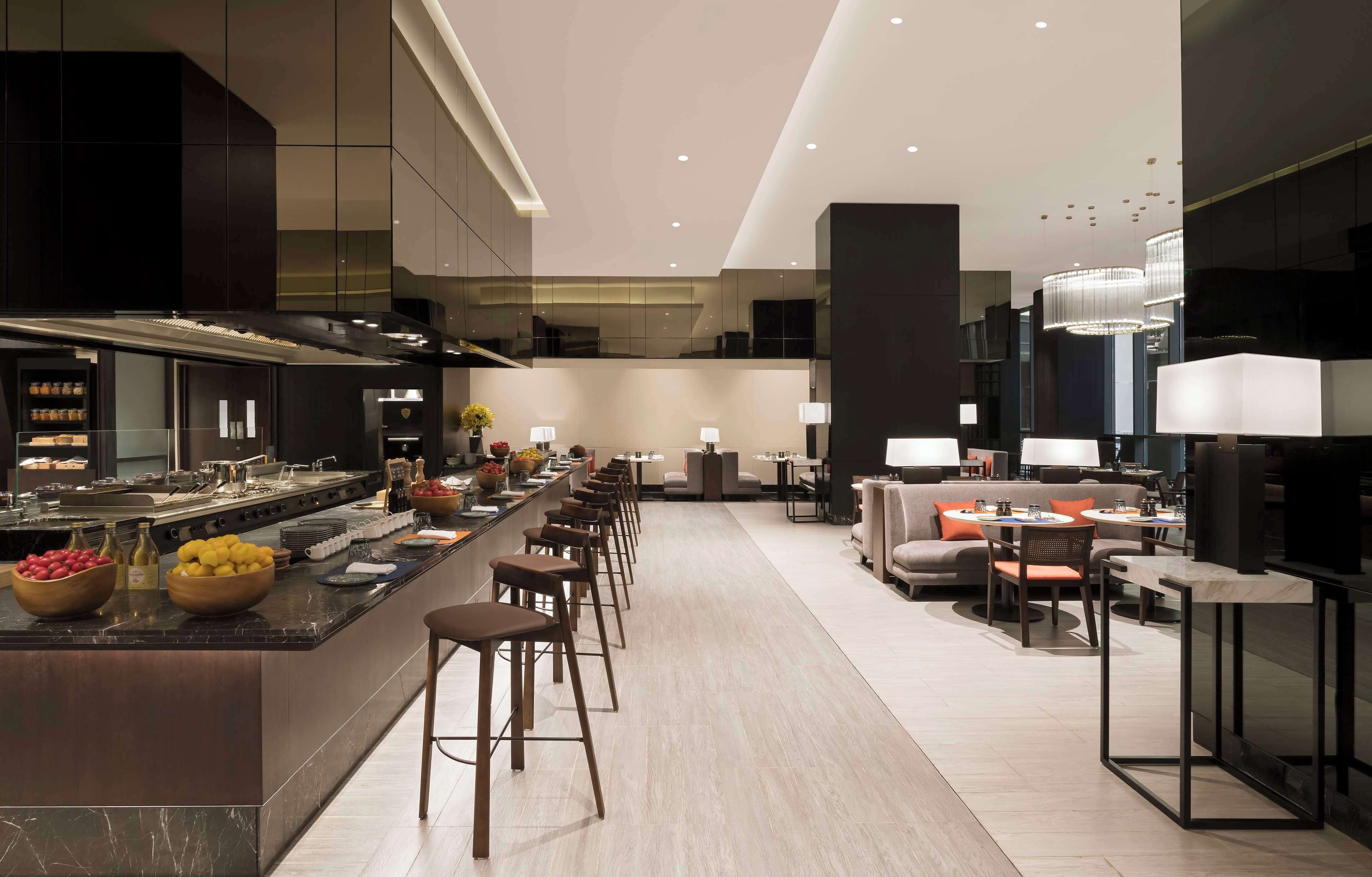 Una cocina moderna con una isla central, asientos tipo bar y un comedor con sofás y mesas.