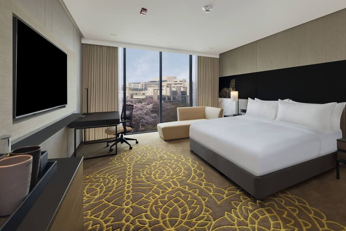 Une chambre d’hôtel moderne, dotée d’un grand lit, d’un bureau, d’une télévision et offrant une vue sur la ville.
