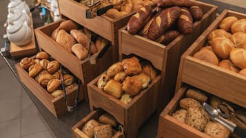 Expositores de madeira repletos de produtos de panificação como pão, bolos e croissants.