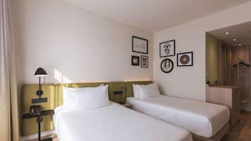 Habitación de hotel con dos camas, una mesita de noche con lámpara, teléfono y cuadros en la pared.