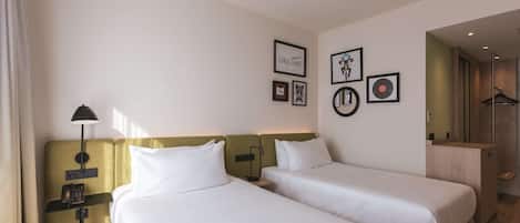 Habitación de hotel con dos camas, una mesita de noche con lámpara, teléfono y cuadros en la pared.