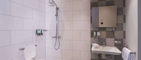 A modern bathroom with white tiles, a shower, a toilet, and a sink.