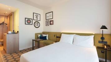 A hotel room with a large bed, a desk, a chair, a wardrobe, and a wall with framed pictures.