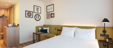 Una habitación de hotel con una cama grande, un escritorio, una silla, un armario y una pared decorada con cuadros.
