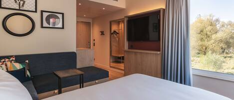 Habitación de hotel con una cama grande, un sofá, una mesita, un televisor y una ventana con cortinas.