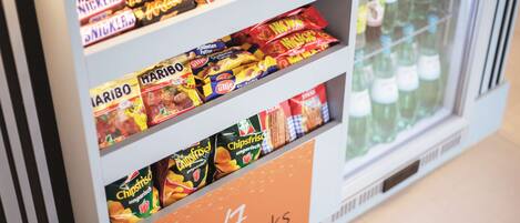 A snack display with various brands and a sign indicating '24/7 snacks' available.