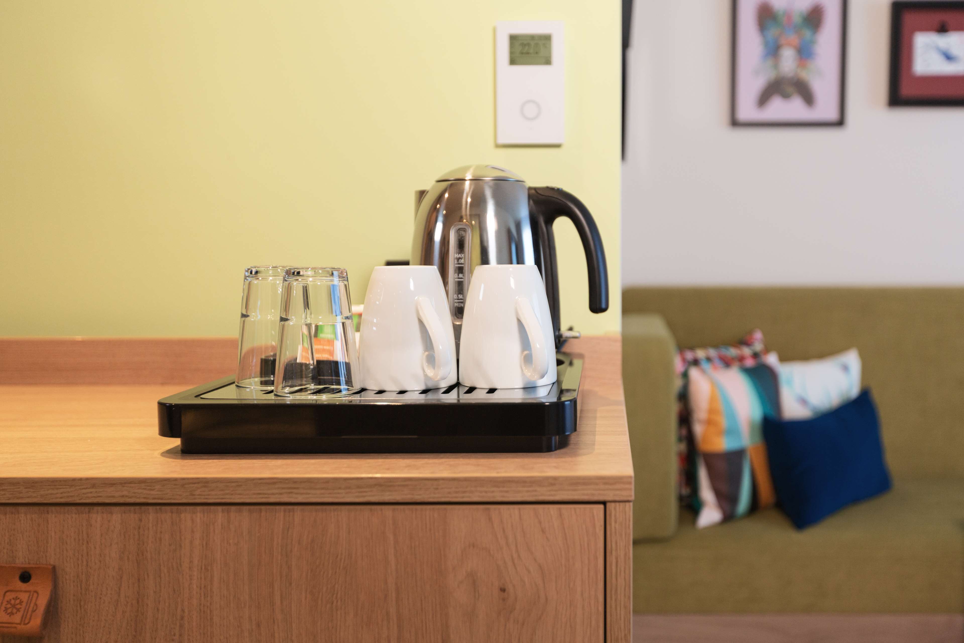 A coffee maker on a wooden counter with two white cups and two clear glasses.