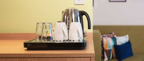 A coffee maker on a wooden counter with two white cups and two clear glasses.
