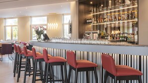 A bar area with a long counter, multiple stools, and a well-stocked shelf of bottles. - Hampton by Hilton Konstanz (Konstanz)