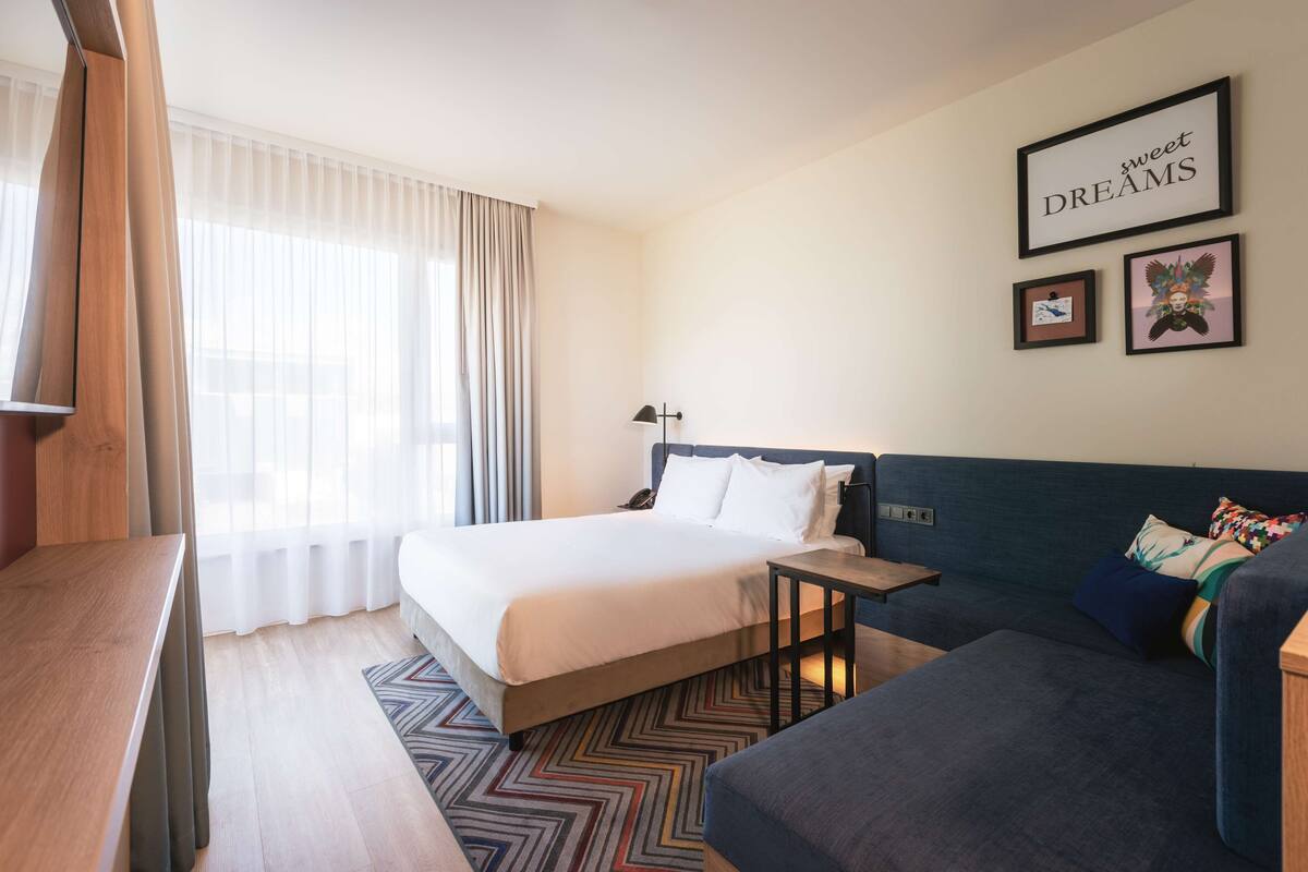 A hotel room with a bed, a sofa, a desk, and a wall with framed pictures.