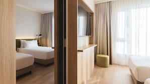A hotel room with two beds, a desk, a TV, and a window with curtains. - Hampton by Hilton Konstanz (Konstanz)
