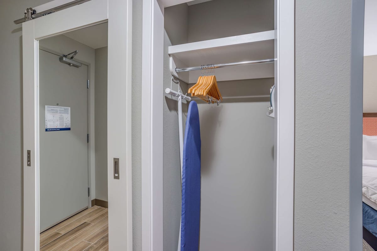 A hotel room with a shower, a towel rack with a blue towel and an orange hanger, and a bed with white bedding.