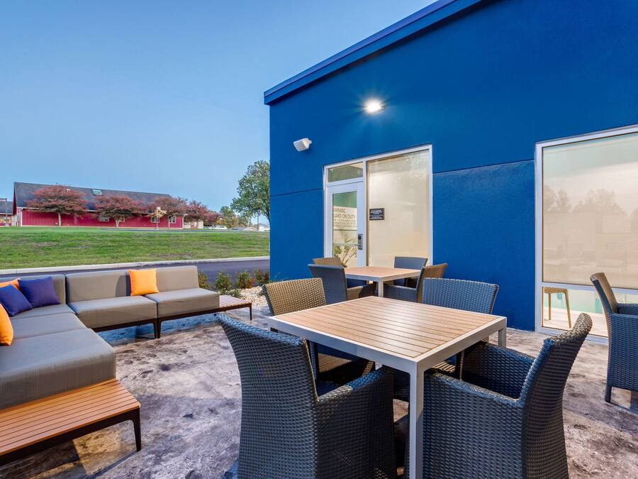 An outdoor seating area with a blue building, a wooden table, and wicker chairs.
