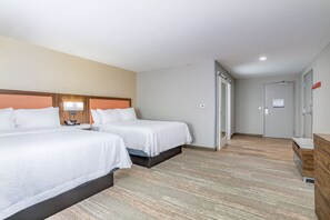 Habitación de hotel con dos camas, cabecera de madera, escritorio con lámpara y puerta que da a otra habitación.