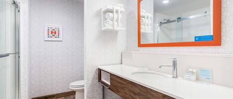 A modern bathroom with a glass shower enclosure, a white toilet, and a vanity with a wooden countertop and a large mirror.