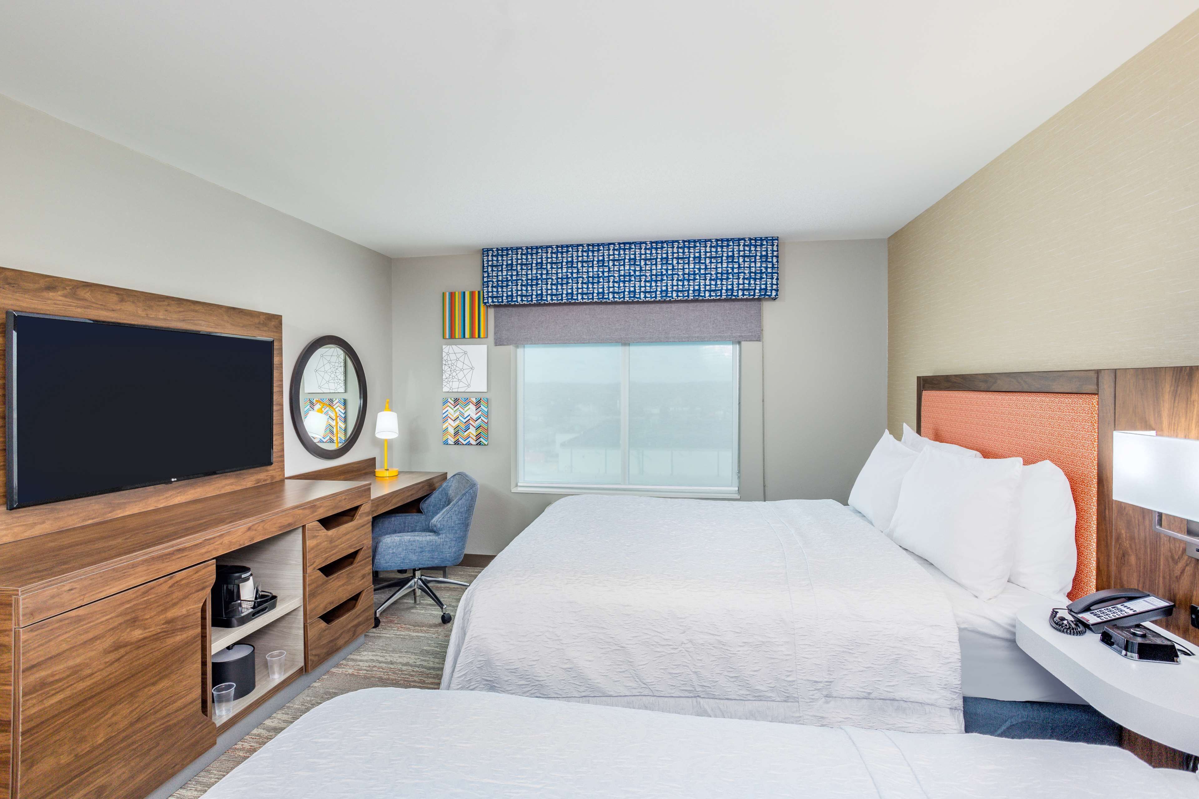A hotel room with a large bed, a TV, a desk with a phone, and a window with a view.