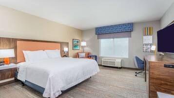 A hotel room with a large bed, a desk, a chair, a lamp, and a window.