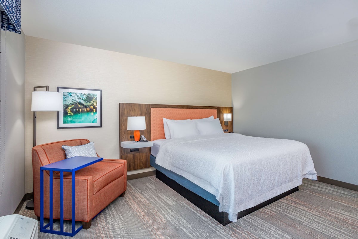 A hotel room with a bed, a sofa, a nightstand, a lamp, and a framed picture on the wall.