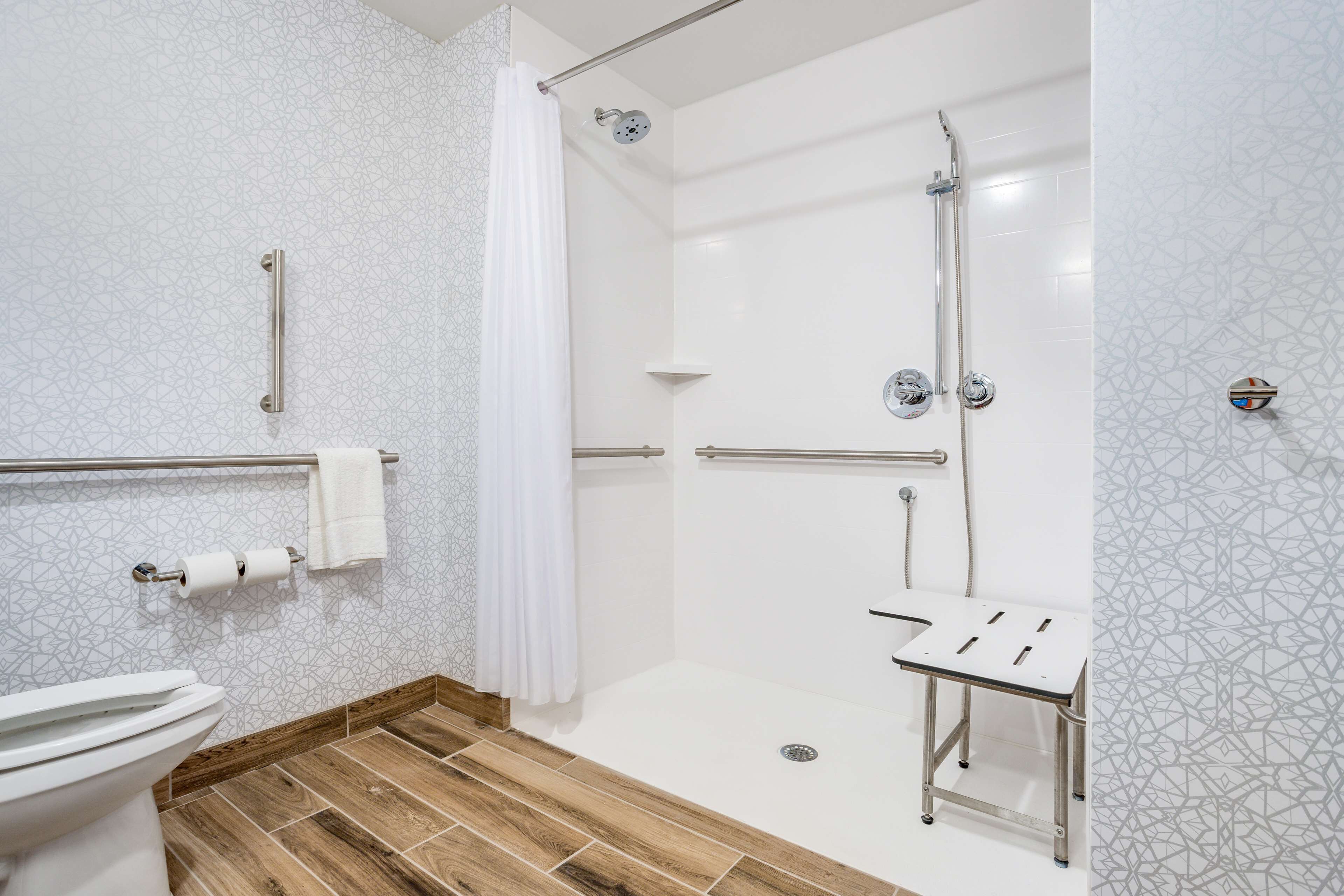 A modern bathroom with a shower, toilet, and a grab bar.